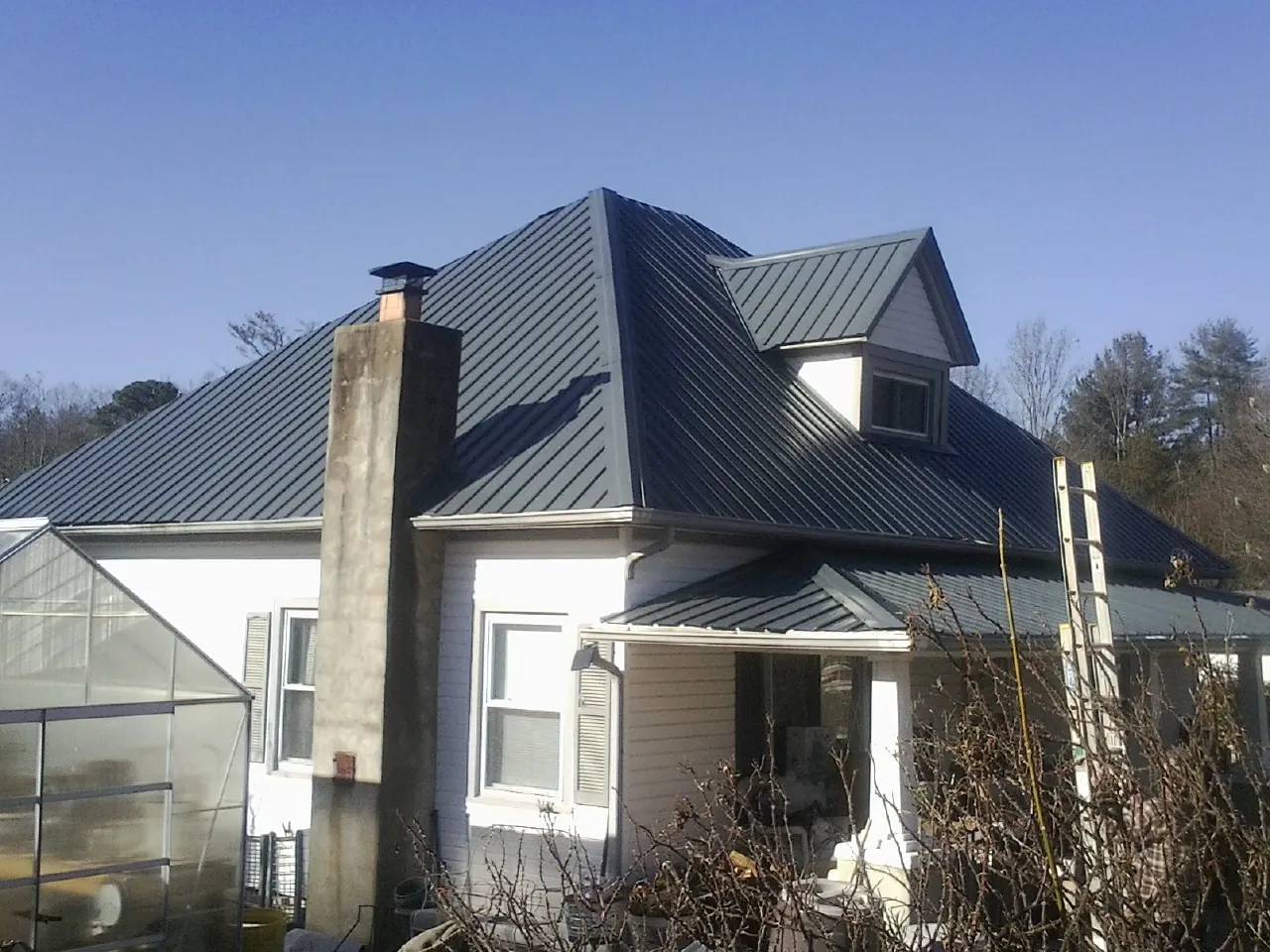 Dark blue standing seam metal roof on a white farmhouse with dormer — Slate & Tile Roof Repair by Roofing Brothers in Guin