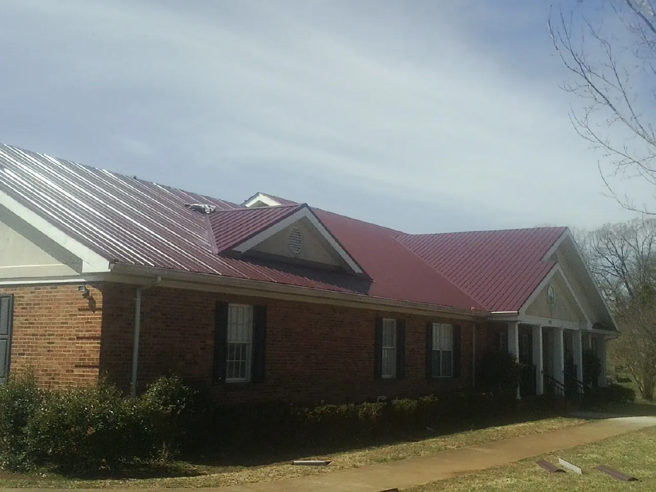 Red metal roof with gabled entries on a long brick building, from a Hail Damage Roof Repair job in Guin