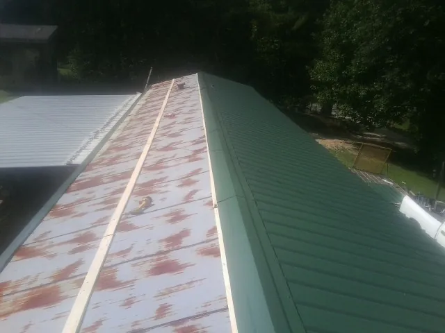 Old rusted panels beside newly installed green metal roofing — Wind Damage Roof Repair by Roofing Brothers in Guin