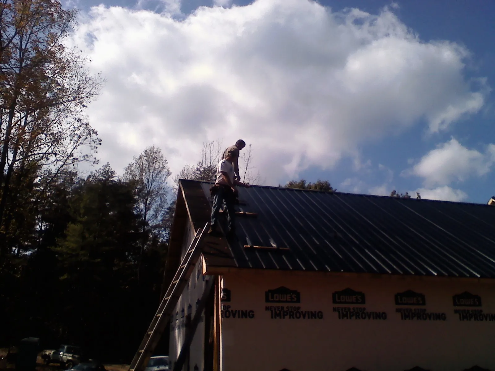 Roofer fastening dark metal panels high against a cloudy sky, from a Roof Inspection job in Guin