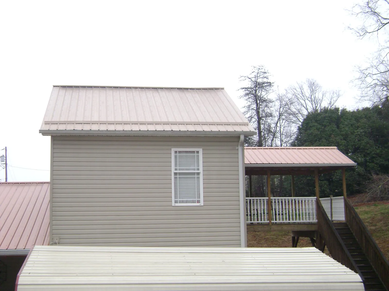 Tan metal roofs on a two story addition and attached porch, from a Roof Replacement job in Guin